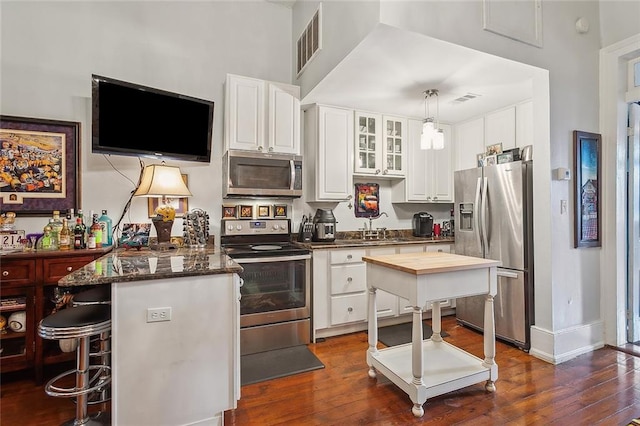 kitchen featuring dark wood-type flooring, appliances with stainless steel finishes, decorative light fixtures, a kitchen island, and white cabinetry