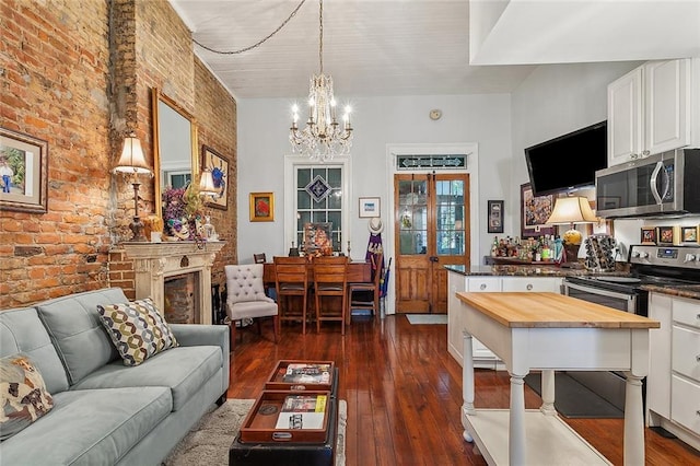 living room featuring french doors, a fireplace, dark hardwood / wood-style flooring, brick wall, and a chandelier