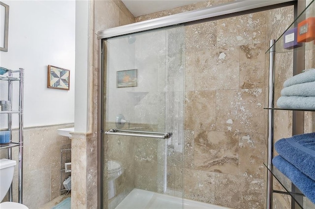 bathroom featuring toilet, a shower with shower door, and tile walls