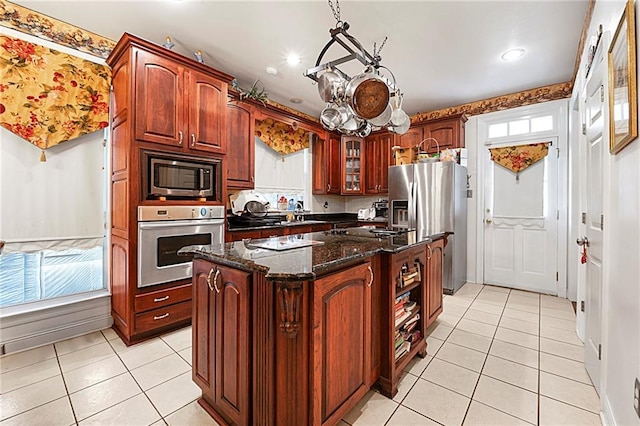 kitchen featuring appliances with stainless steel finishes, a center island, light tile patterned floors, and dark stone countertops