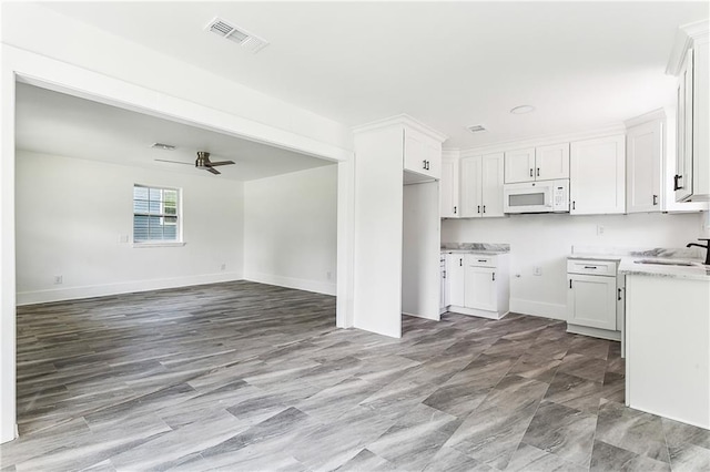 8014 Lucerne St, New Orleans, LA 70128 - kitchen with white microwave, open floor plan, a sink, white cabinetry, and a ceiling fan