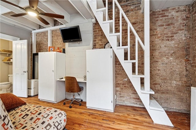 basement featuring light hardwood / wood-style flooring, ceiling fan, and brick wall