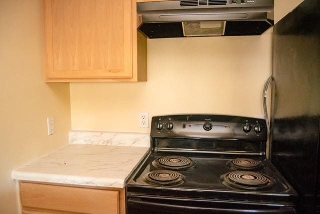 kitchen featuring ventilation hood, black stove, light brown cabinetry, and fridge