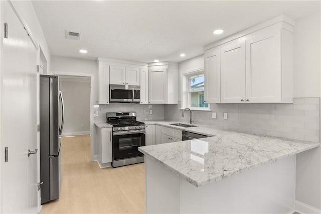 kitchen featuring kitchen peninsula, appliances with stainless steel finishes, light stone counters, sink, and white cabinetry