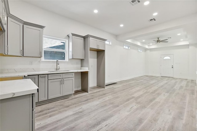 kitchen with light wood-type flooring, gray cabinets, ceiling fan, and sink