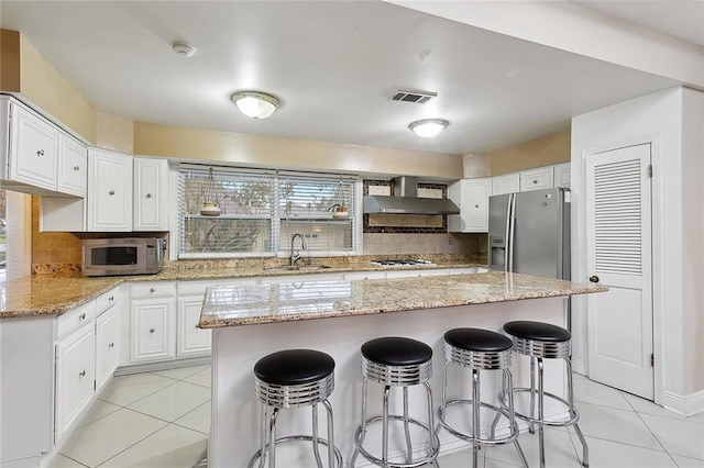 kitchen featuring appliances with stainless steel finishes, a center island, white cabinetry, and wall chimney range hood