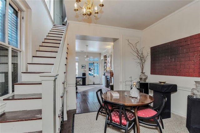 dining room with ornamental molding, ceiling fan with notable chandelier, and dark wood-type flooring