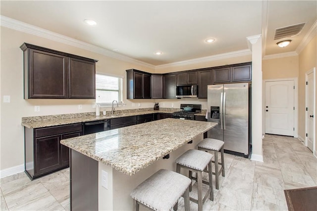 kitchen featuring a breakfast bar, black appliances, sink, ornamental molding, and a kitchen island