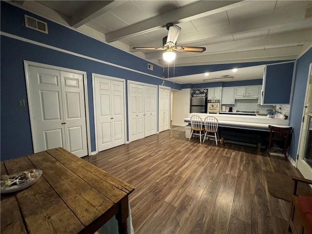 interior space with stainless steel fridge, ceiling fan, dark wood-type flooring, beamed ceiling, and white cabinets