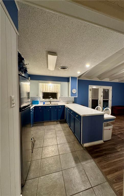 kitchen featuring a textured ceiling, blue cabinets, kitchen peninsula, and light tile patterned floors