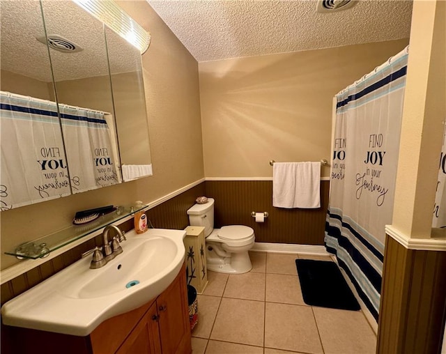 bathroom with tile patterned floors, vanity, a textured ceiling, wooden walls, and toilet