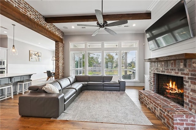 living room featuring crown molding, dark hardwood / wood-style floors, ceiling fan, a fireplace, and beam ceiling