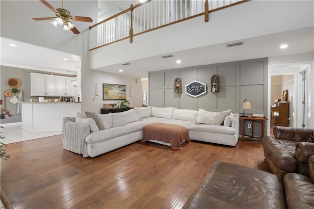 living room with a towering ceiling, hardwood / wood-style flooring, and ceiling fan