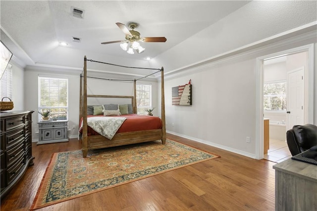 bedroom with hardwood / wood-style floors, ensuite bathroom, ceiling fan, and a raised ceiling