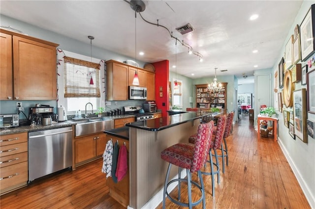 kitchen with sink, hardwood / wood-style floors, pendant lighting, a kitchen island, and appliances with stainless steel finishes