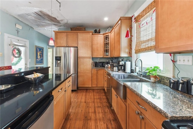 kitchen with sink, hanging light fixtures, dark hardwood / wood-style floors, dark stone countertops, and appliances with stainless steel finishes