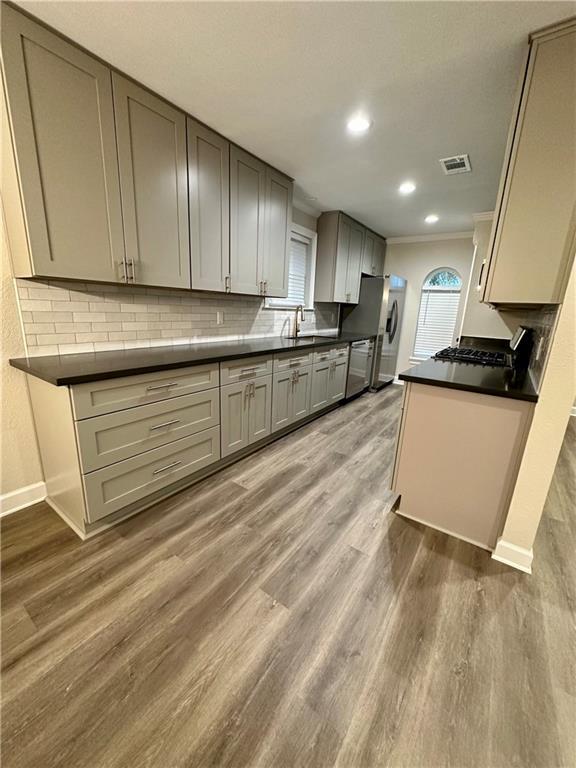 kitchen with gray cabinetry, backsplash, dark wood-type flooring, crown molding, and appliances with stainless steel finishes