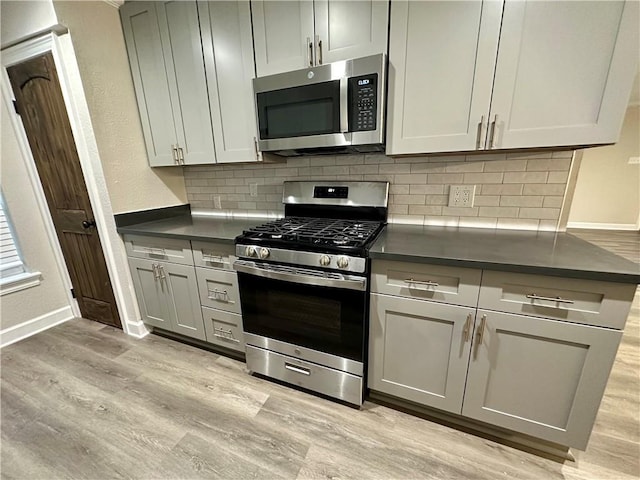 kitchen with backsplash, gray cabinets, stainless steel appliances, and light wood-type flooring