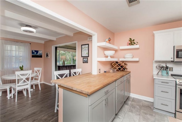 kitchen featuring decorative backsplash, gray cabinets, a breakfast bar, and appliances with stainless steel finishes