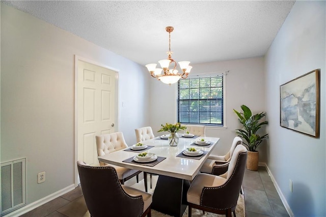 dining area with dark tile patterned floors, a textured ceiling, and an inviting chandelier