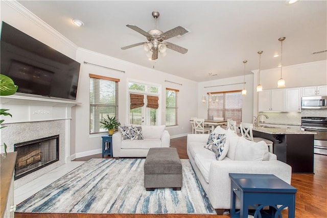 living area with a fireplace with flush hearth, baseboards, wood finished floors, ceiling fan, and ornamental molding