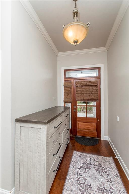 doorway featuring baseboards, dark wood-type flooring, and crown molding