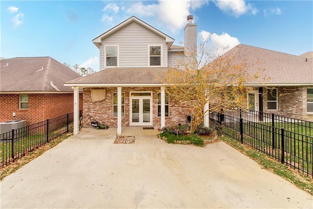 rear view of property featuring central air condition unit, a chimney, french doors, a fenced backyard, and brick siding