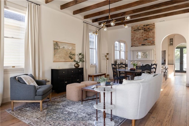 living area featuring beamed ceiling, arched walkways, a healthy amount of sunlight, and hardwood / wood-style floors