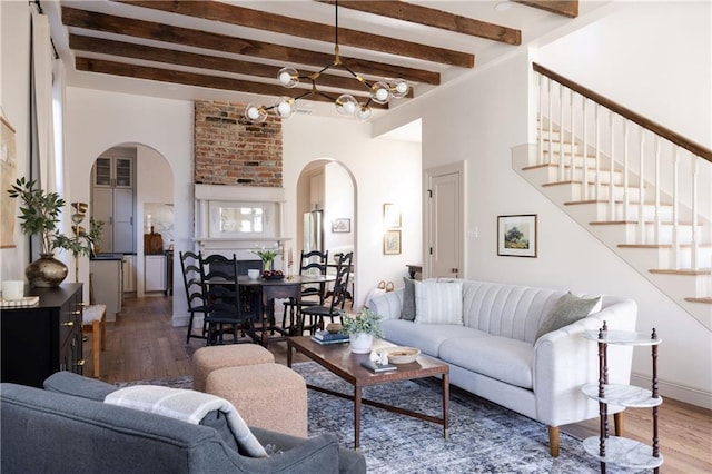 living room with an inviting chandelier, stairway, wood finished floors, and arched walkways