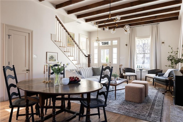 dining room featuring beamed ceiling, light wood-style floors, an inviting chandelier, and stairs