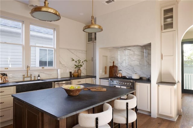 kitchen with dark countertops, a center island, glass insert cabinets, appliances with stainless steel finishes, and hardwood / wood-style flooring