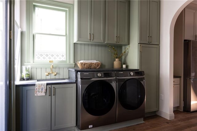 laundry room featuring wood finished floors, cabinet space, arched walkways, a sink, and independent washer and dryer