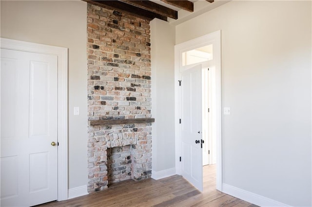 unfurnished living room with beamed ceiling, baseboards, wood finished floors, and a fireplace