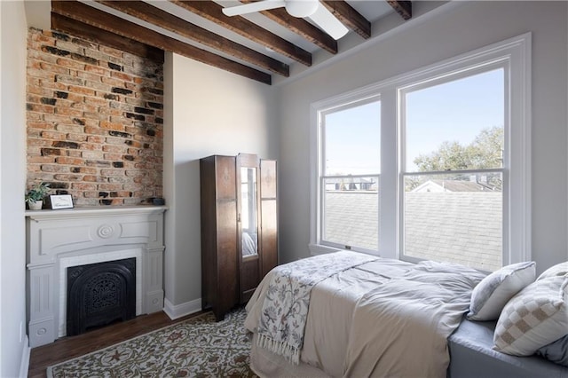 bedroom with beam ceiling, wood finished floors, and a fireplace