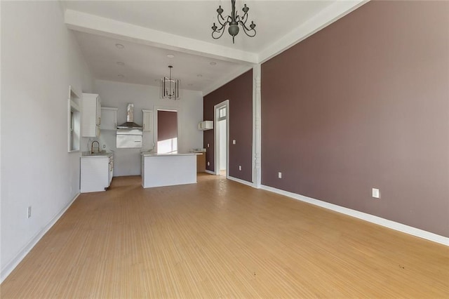 unfurnished living room featuring beamed ceiling, light wood-type flooring, sink, and an inviting chandelier