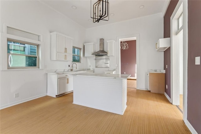 kitchen featuring white cabinets, wall chimney range hood, hanging light fixtures, and a chandelier