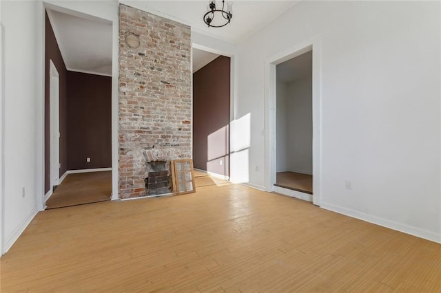 unfurnished living room with a brick fireplace, a chandelier, and light wood-type flooring