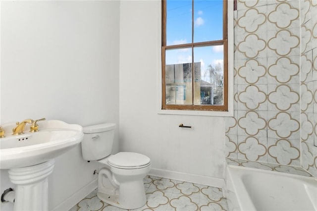 bathroom with tile patterned floors, a tub to relax in, toilet, and sink