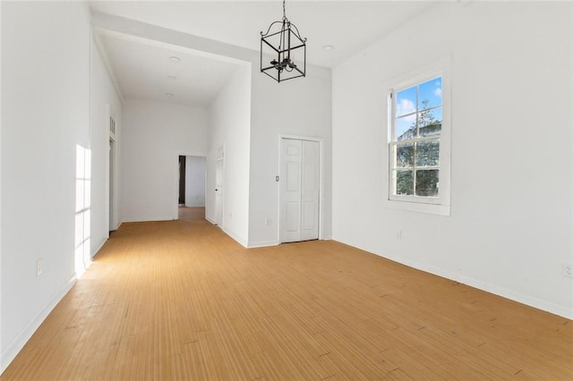 spare room with a high ceiling, an inviting chandelier, and light hardwood / wood-style flooring