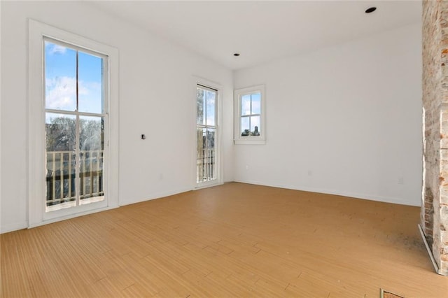 unfurnished room with light wood-type flooring, a stone fireplace, and plenty of natural light