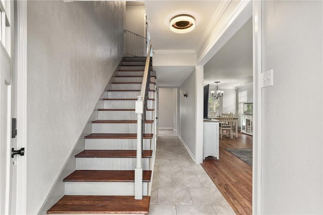 staircase featuring wood-type flooring, ornamental molding, and a chandelier