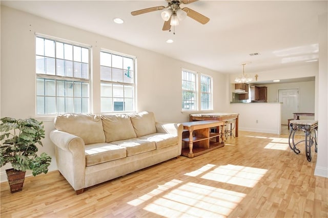 living room featuring ceiling fan with notable chandelier and light hardwood / wood-style flooring