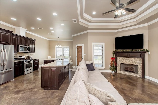 kitchen with light stone countertops, sink, crown molding, a center island with sink, and appliances with stainless steel finishes