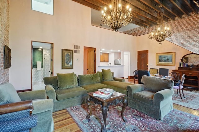 living room with beamed ceiling, a towering ceiling, light hardwood / wood-style floors, and brick wall