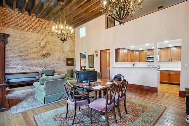 dining room featuring beamed ceiling, brick wall, light hardwood / wood-style floors, and a high ceiling