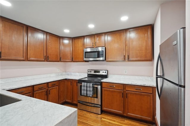 kitchen featuring light hardwood / wood-style floors, light stone countertops, and appliances with stainless steel finishes