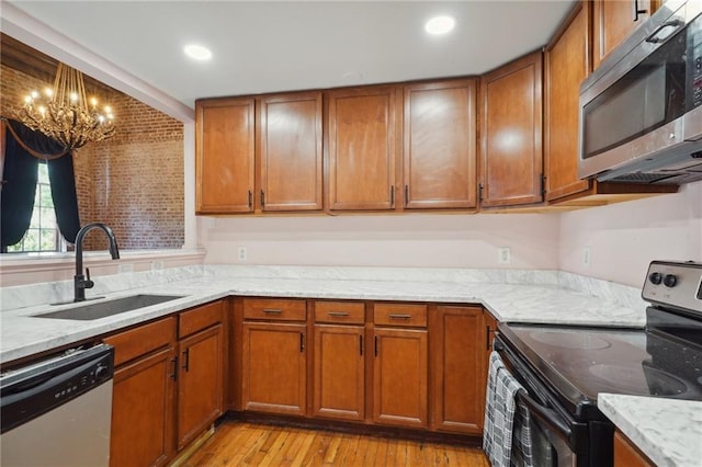 kitchen featuring sink, stainless steel appliances, light stone counters, a chandelier, and light hardwood / wood-style floors