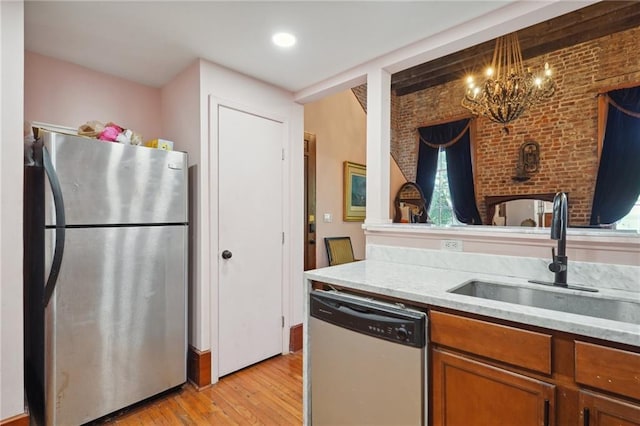 kitchen with sink, light hardwood / wood-style flooring, appliances with stainless steel finishes, a notable chandelier, and brick wall