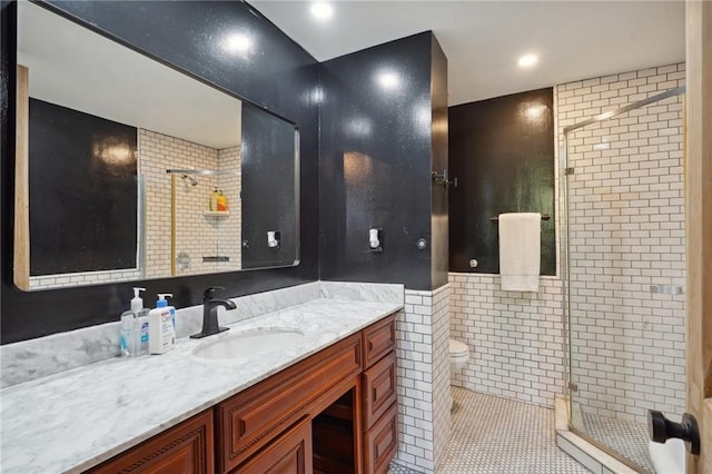 bathroom with tile patterned floors, toilet, vanity, a shower with shower door, and tile walls