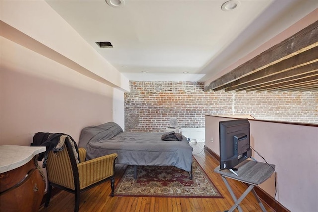 bedroom featuring hardwood / wood-style floors and brick wall